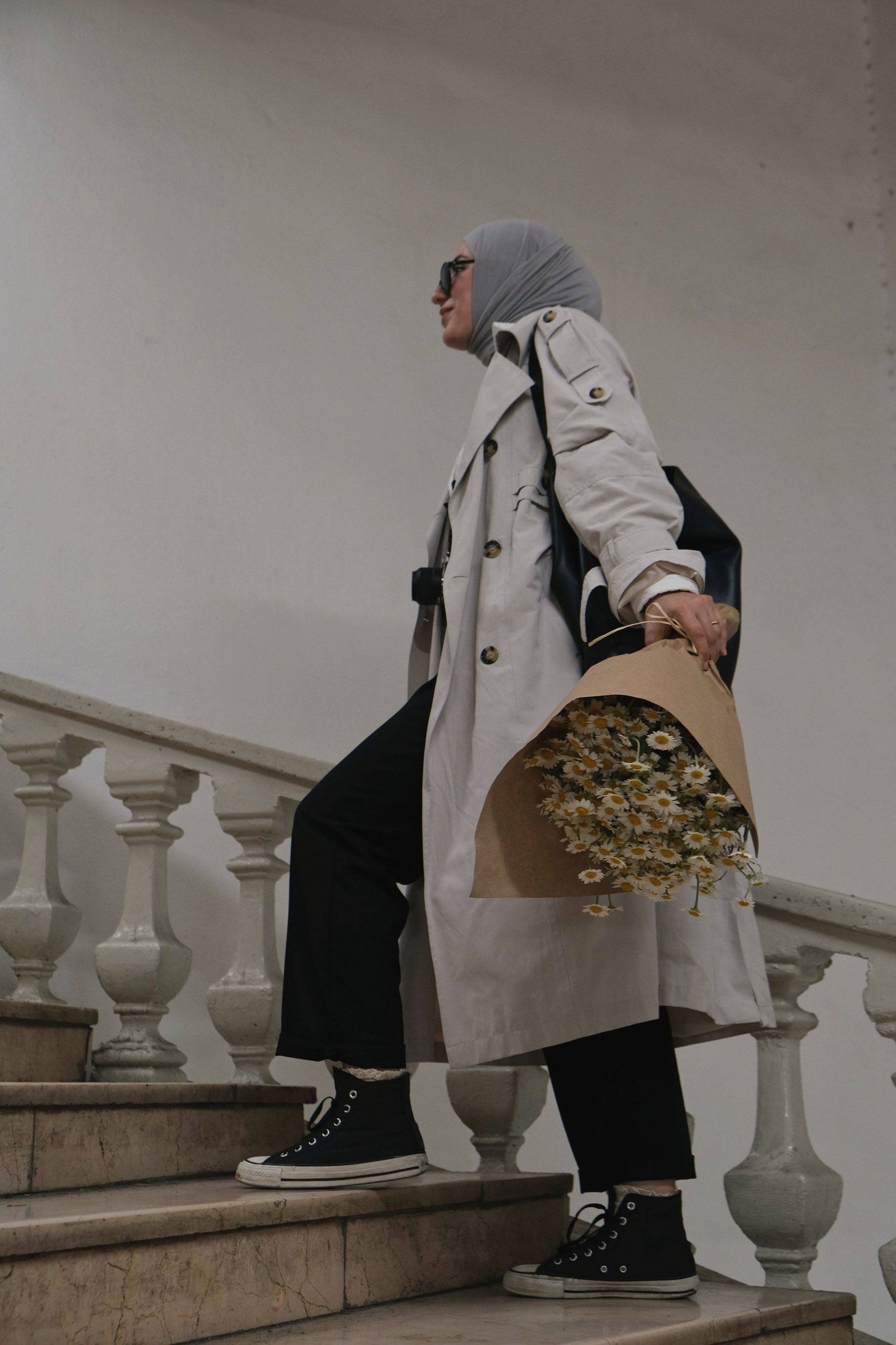 Someone walking down pale stone stairs, a wrapped bouquet tucked under their arm
